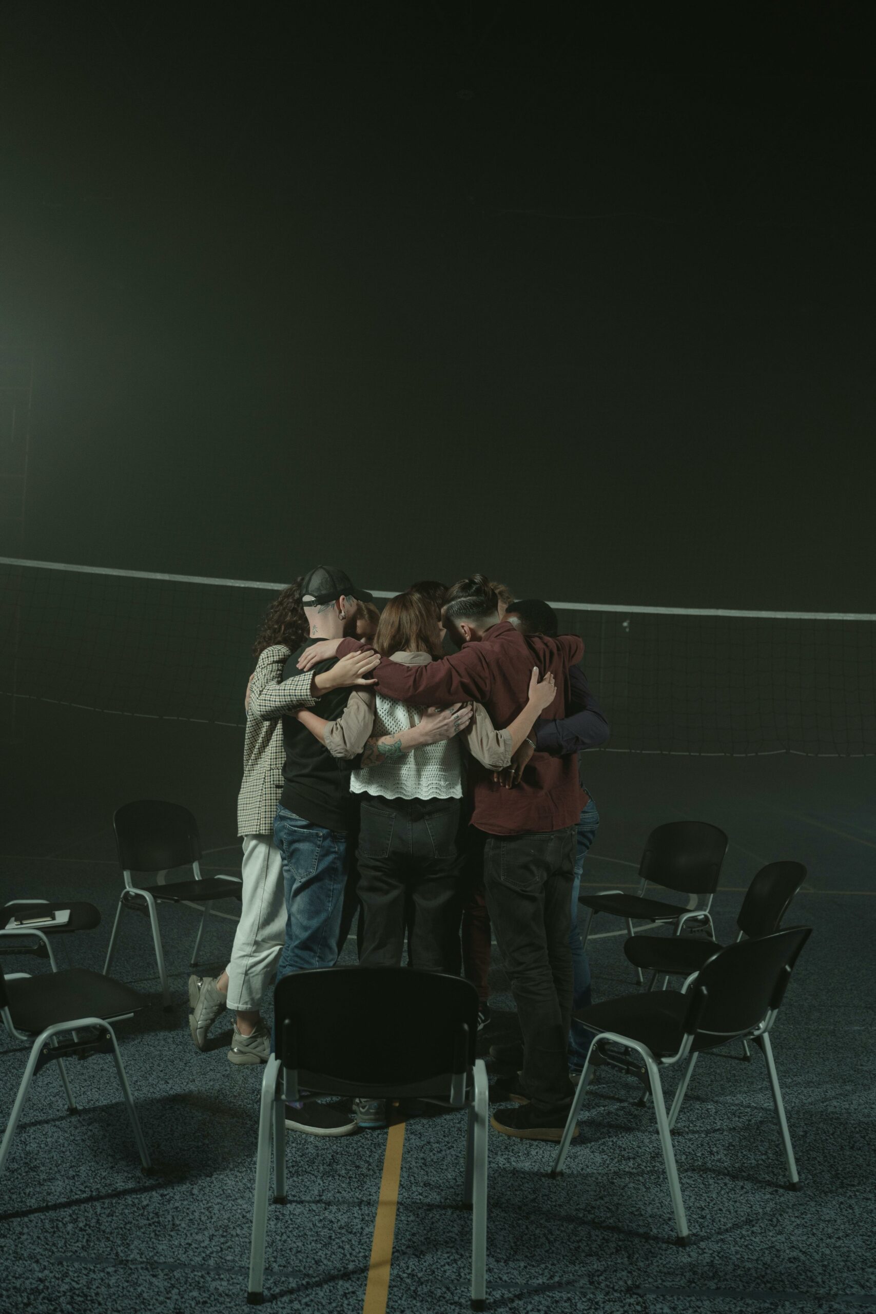 A small group of diverse adults embracing in a supportive circle indoors, symbolizing unity and support.